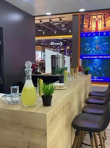Fuar standında limonata sürahisi, bardaklar ve bar tabureleriyle ikram barı